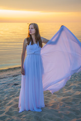 Beautiful girl in a long white dress walking on the seaside.