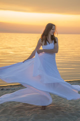 Beautiful girl in a long white dress walking on the seaside.