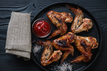 Frying pan with bbq chicken wings on a black wooden background