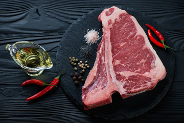 Raw club beefsteak with seasonings over black wooden surface