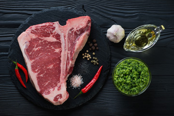Raw club beef steak with spices, olive oil and chimichurri sauce