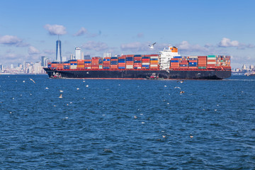 Fototapeta premium View of the New York Skyline with a freighter boat passing in front of the buildings.