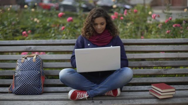 Young mixed race lady writing essay on laptop, studying, full of inspiration