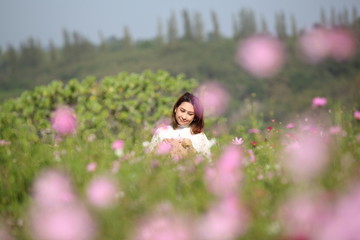 Fototapeta na wymiar Beautiful young woman in a field of Purple, pink, red, cosmos flowers in the garden with blue sky and clouds background in vintage style soft focus.