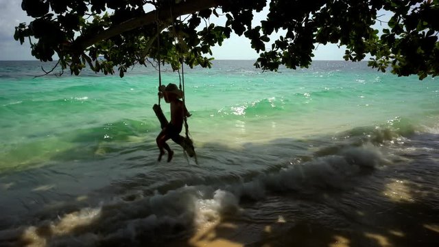 A boy playing on a swing on a beach located on the island Koh Kradan in southern Thailand.