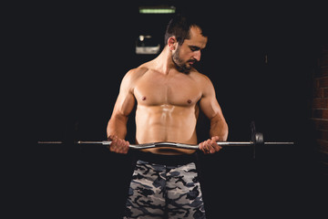Athlete lifting a curl bar with weights isolated in an almost completely dark room