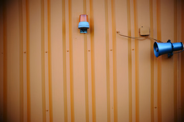 Warnsignale / Ein alter und zerbeulten Lautsprecher sowie eine Warnleuchte an einer Wellblechwand.