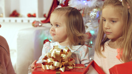 Fototapeta premium Happy family with two young daughters at the Christmas tree with gifts