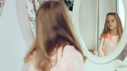 Fashionable little lady combing her hair and looking in the mirror