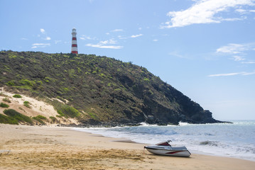 A far view of a lighthouse a top of a hill in some beach in the middle of the day.