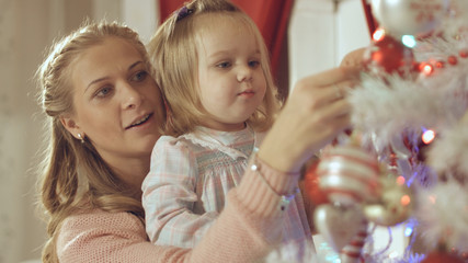Mother with adorable baby decorate a Christmas tree at home