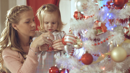 Mother with adorable baby decorate a Christmas tree at home