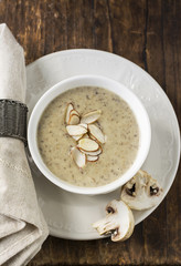 Cream soup with mushrooms in a white ceramic dish served  almond petals. selective Focus