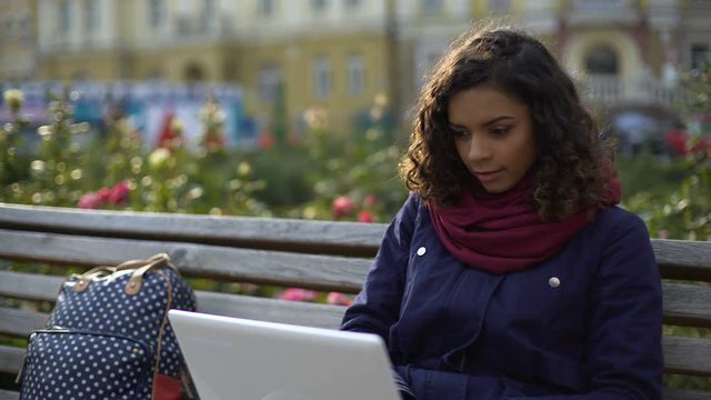 Young biracial writer working on new project, sitting with laptop outdoors