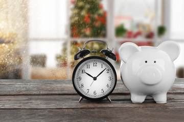 Holiday expenses concept. Piggy bank with alarm clock on wooden table