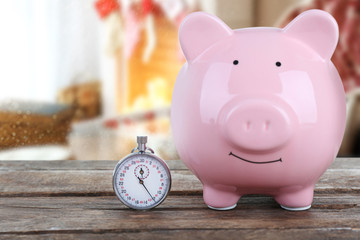 Holiday expenses concept. Piggy bank with stopwatch on wooden table
