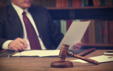 Brown gavel on wooden table and male lawyer on background, close up view