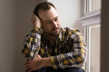 Handsome depressed man sitting near window