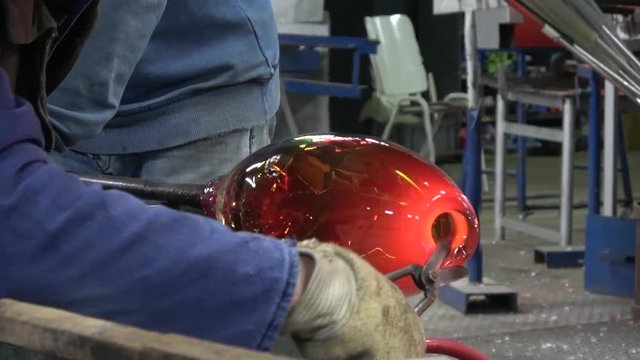 Footage of glassblowing workshop factory glassblower also known as glassmith or gaffer cutting of not needed glass vase while turning glass crystal from oven is glowing yellow orange from heat 4k