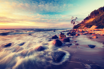 Sea landscape at sunset, sandy beach and cliff,waves breaking on - obrazy, fototapety, plakaty