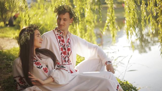 young couple in love on the shore of the river on a romantic date. Guy and girl in the embroidered shirts near the willows on the river bank