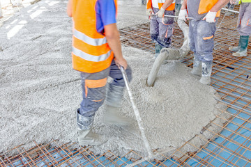 Workers are spreading concrete over big reinforced floor on the