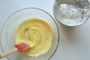 Mixing batter for a sponge cake in a glass bowl - egg yolks with sugar and egg whites into stiff peaks