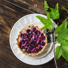 Homemade tart from the pastry with black currant and cream filling on a dark wooden background. Top view