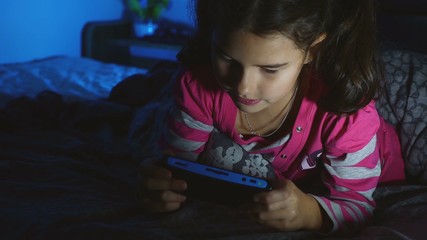 teen kid girl playing a portable video game console at night indoors