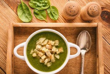 Green cream vegetable soup with croutons on wooden tray.