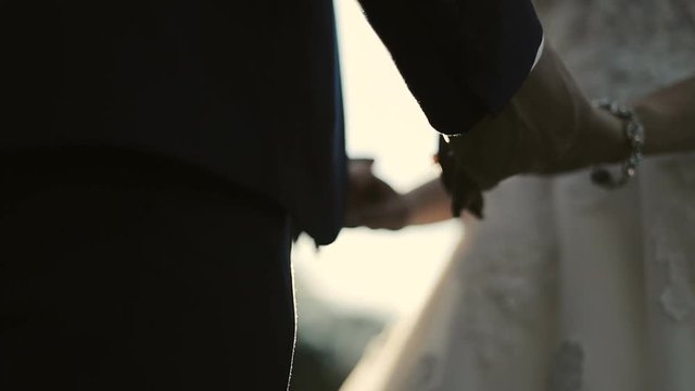 Outdoor shot of a young wedding couple, bride and groom, hand holding against sunset
