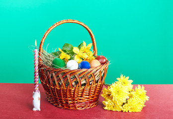 Easter basket with flowers and Easter eggs near a burning candle