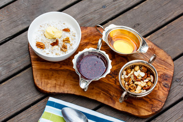 Oatmeal in a bowl, stand near the bowl honey, jam, nuts and brea
