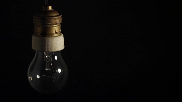 Una vecchia lampada al tungsteno, si accende e si spegne in modo intermittente veloce, su fondo nero.