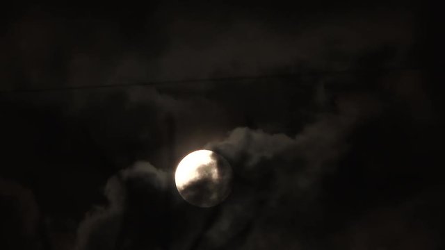Rare Christmas day full moon time lapse rising through cloud layers with winter tree branches in foreground.