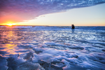 Winter Adventure. A young photographer shooting a sunset on a frozen lake. Port Austin, Michigan.