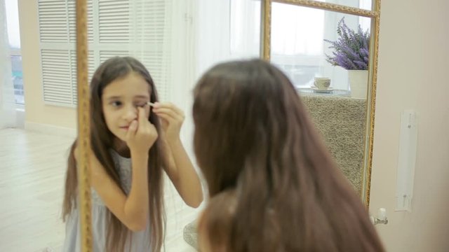 little girl is painted before a mirror her mother's makeup