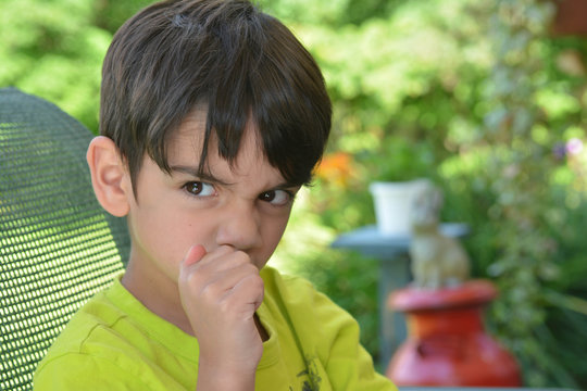 Young angry mischievious boy sitting on chair on a sunny day.