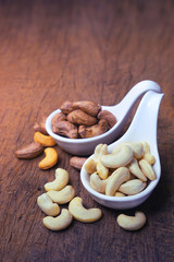 cashew nuts and roasted salt cashew nut in shell on white ceramic spoon.