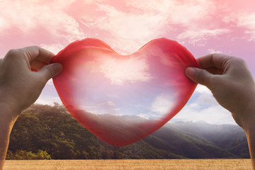 hands hold big red heart in romantic nature view