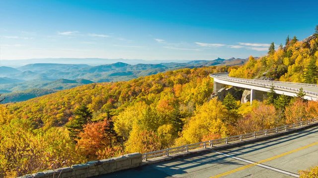 Panning from Layered Blue Ridge Mountains to Linn Cove Viaduct at Grandfather Mountain near Linville NC with Vehicle Traffic on a Sunny Autumn Morning Surrounded by Fall Colored Trees and a Blue Sky