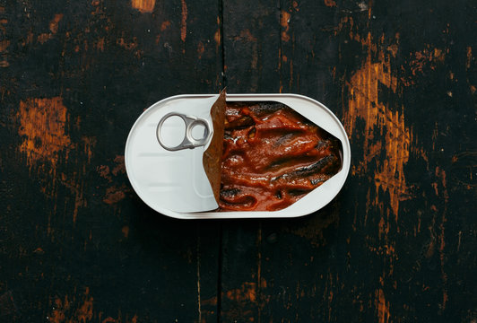 open canned sprats in tomato sauce on an old black wooden table closeup, top view