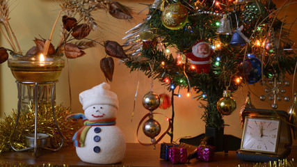 It is almost midnight hour! An arrangement with snowman figure, Christmas tree with presents at the foot of it, table clock, burning floating wick, wheat, seedpods of the Goldenraintree and garland.