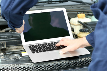 Mechanic standing in front of an open car hood with laptop