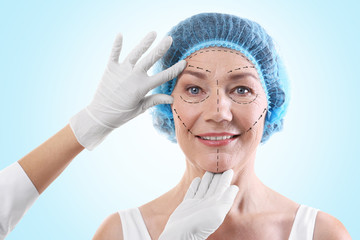 Surgeon examining female face against blue background. Plastic surgery concept