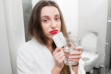 Sick woman with headache holding pills and glass of water in the bathroom