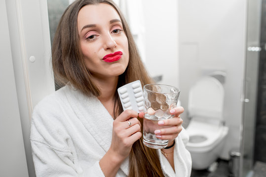 Sick woman with headache holding pills and glass of water in the bathroom