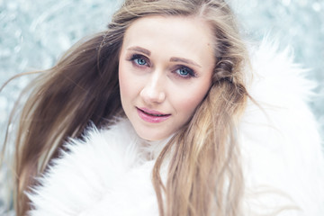 Young woman in white fur coat against wall of shattered mirrors.