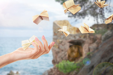 Female hand and flying books on landscape background