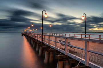 Illuminated wooden pier in Gdynia Orlowo with blurred clouds on the sky. Poland.